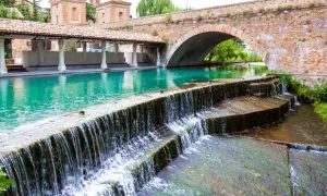 Cascata d'acqua cristallina sotto un antico ponte in mattoni, un angolo di pace tra i borghi medievali umbri.