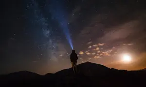 Persona su una montagna di notte, illuminata da una torcia, sotto un cielo stellato mozzafiato.