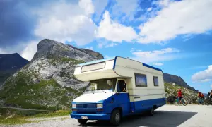 Camper blu e bianco parcheggiato in montagna, pronto per esplorare gli **itinerari camper Italia**. Due ciclisti sullo sfondo.