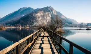 Passerella in legno su lago calmo, montagne sullo sfondo. Un luogo incantevole per scoprire cosa vedere in Franciacorta.
