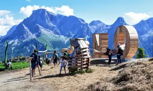 Un'estate a San Martino di Castrozza: bambini giocano in un parco avventura con sculture in legno e montagne maestose sullo sfondo.