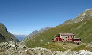 Rifugio nel Val di Rhemes, con persone sedute ai tavoli all'esterno, circondato da verdi pendii montuosi sotto un cielo azzurro.