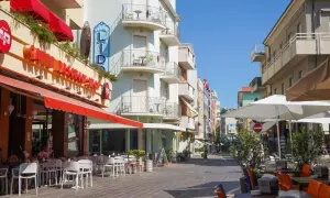 Passeggiata serale a Gabicce Mare: tavolini all'aperto di un caffè, hotel Lido e negozi colorati.
