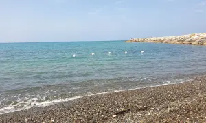 Spiaggia di ciottoli a Cecina, con mare calmo e un molo in lontananza. Perfetto per scoprire cosa vedere e rilassarsi.