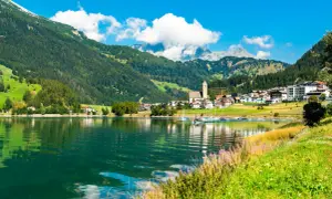 Incantevole lago alpino con barche a vela, circondato da verdi montagne e pittoreschi borghi Trentino Alto Adige.