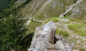 Sentiero lastricato su un versante montuoso, con un tronco di legno che spunta dalla pietra. Un percorso che ricorda le antiche vie, come quelle delle **via Vandelli tappe**.
