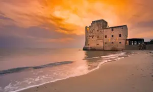Spiaggia Torre Mozza Follonica: tramonto dorato su antica fortezza sul mare. Come arrivare: facile accesso dalla strada costiera.