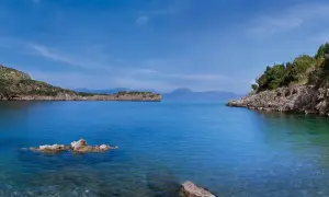 Calmo mare a maggio, con scogli affioranti e coste verdi sotto un cielo azzurro.
