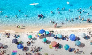 Viste aeree di spiagge di sabbia con fondale basso in Calabria, con bagnanti che si godono il sole e il mare cristallino.