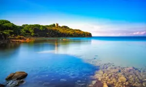 Torre medievale su una collina verdeggiante che si affaccia su acque cristalline, una delle punta ala spiagge più belle.