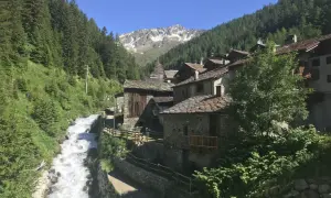 Un pittoresco borgo alpino nel Nord Italia, con case in pietra e tetti in ardesia, incastonato tra boschi rigogliosi e un torrente impetuoso.