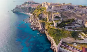 Fortificazioni storiche su una costa rocciosa con mare blu intenso. Un'idea per cosa visitare in Toscana in 2 giorni, tra storia e natura.