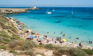 Spiaggia di Favignana, dove si trova questo paradiso azzurro con gente che si gode il sole e il mare cristallino, con barche all'orizzonte.