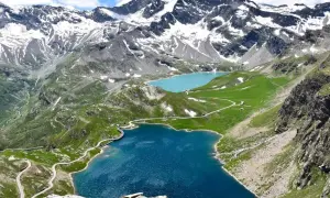 Laghi alpini e strada tortuosa sul colle del Nivolet, con montagne innevate sullo sfondo.
