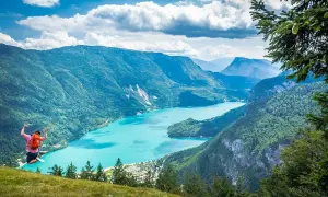 Giovane salta felice con zaino rosso, godendosi le passeggiate facili vicino a Trento con vista su lago turchese e montagne verdi.