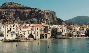 Un incantevole borgo da visitare in Sicilia, con case color pastello affacciate sul mare azzurro e una scogliera imponente alle spalle.