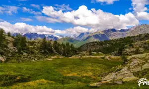 Val Seriana: un prato verde e rocce ai piedi di montagne innevate, ideale per passeggiate facili e rigeneranti.