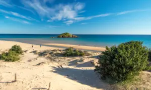 Dune sabbiose e mare turchese, un'isola rocciosa in lontananza. Un assaggio delle spiagge più belle Sardegna, con persone che passeggiano sulla riva.