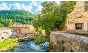 Un ruscello attraversa un borgo umbro con case in pietra e vegetazione lussureggiante. Una cartina ideale per scoprire i borghi dell'Umbria.