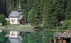 Suggestiva chiesa nel lago trentino, con riflessi sull'acqua verde smeraldo e un pontile in legno con barche.