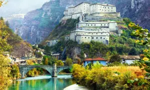 Fortezza imponente su un colle, con un fiume turchese e un ponte ad arco. Un paesaggio da fiaba tra Piemonte e Valle d'Aosta.