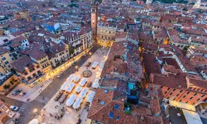 Vista aerea di piazza Erbe a Verona, con i suoi edifici storici, la torre e i tavolini all'aperto.