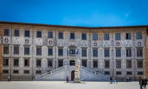 Palazzo della Sapienza a Pisa, con la sua facciata decorata, si affaccia su una piazza dove si intravede la **torre di Pisa** in lontananza, nella **Piazza del Duomo, Pisa, PI**.