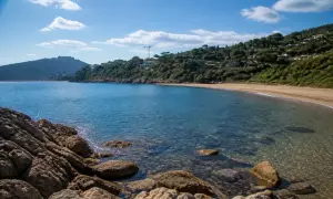 Baia tranquilla con acque cristalline e sabbia dorata, una delle splendide porto ercole spiagge, incorniciata da rocce e vegetazione lussureggiante.