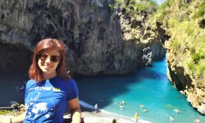 Giovane donna sorride in una baia con acqua turchese, uno dei tanti posti da visitare in Calabria.
