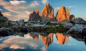 Le Tre Cime di Lavaredo illuminate dal tramonto, riflesse in uno specchio d'acqua. Le **dolomiti più belle** in uno scenario mozzafiato.
