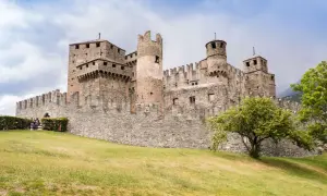 Imponente castello medievale, uno dei borghi Valle d'Aosta più suggestivi, con torri merlate e mura in pietra su un prato verde.