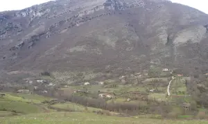 Un paesaggio collinare dove il Cilento mostra case sparse tra alberi spogli e prati verdi, sotto un imponente monte roccioso.