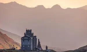 Edificio imponente tra paesaggi di montagna bellissimi, con cime sfumate all'orizzonte e un cielo rosato.