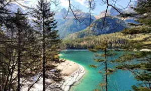 Un lago turchese incastonato tra montagne boscose, con una spiaggia sabbiosa che si estende nel **Val di Non**.