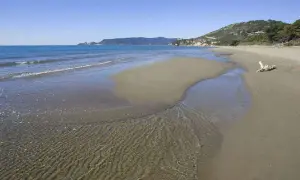 Le **spiagge** dorate dell'**Argentario** incontrano il mare cristallino, con un ruscello che serpeggia sulla **sabbia**.