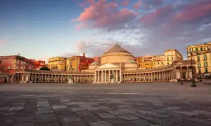 Piazza del Plebiscito a Napoli, con il Palazzo Reale e la Basilica di San Francesco di Paola, sotto un cielo rosato al tramonto.