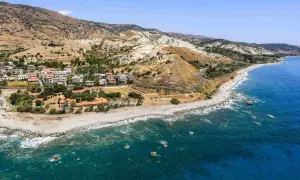 Paesaggio mozzafiato sulla **Calabria Costa Ionica**: case arroccate su colline aride, una spiaggia di ciottoli e il mare blu intenso.