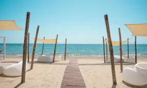 Un percorso in legno conduce al mare cristallino del golfo di Follonica, tra comode sedute bianche e tende parasole.
