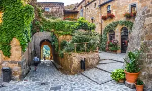 Un vicolo acciottolato tra antichi edifici ricoperti di edera e fiori, un invito a scoprire i borghi da visitare nelle Marche.
