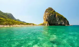 Acque cristalline e un'imponente roccia emergono dal mare bello del Lazio, con colline verdi che si estendono all'orizzonte.