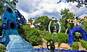 Sculture colorate e fantastiche popolano il **giardino dei tarocchi**, tra alberi verdi e cielo nuvoloso.