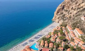Villaggio turistico con spiaggia attrezzata e piscina, incastonato tra il mare blu e una scogliera rocciosa. Un luogo ideale per esplorare i paesi vicino Catania sul mare.