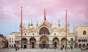 La maestosa Basilica di San Marco a Venezia, con le sue cupole dorate e mosaici scintillanti, si staglia contro un cielo rosa al tramonto.