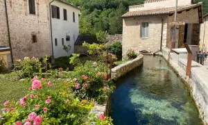 Un ruscello attraversa un borgo umbro, tra case in pietra e rose rosa. Un angolo incantevole tra i borghi più belli dell'Umbria.