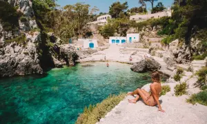 Una donna ammira le acque cristalline di una baia pugliese, con piccole spiagge sabbiose e case bianche arroccate sulla scogliera.
