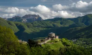 Roccia fortificata nella Garfagnana, dove si trova un castello medievale su una collina verdeggiante, con montagne sullo sfondo.