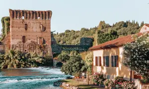 Rovine di un castello medievale e una casa con fiori colorati, un fiume e un ponte: un quadro perfetto dei borghi veneti da visitare.