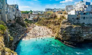 Una baia con spiaggia affollata e case bianche a picco sul mare turchese, una delle splendide spiagge vicino Bari.