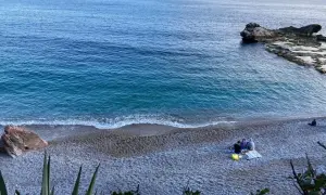 Un mare bello nel nord Italia, con un veliero all'orizzonte e persone che si godono la spiaggia di ciottoli.