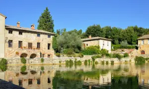 Antica sorgente termale con edifici in pietra e riflessi sull'acqua, un incantevole scorcio dei borghi del Val d'Orcia.